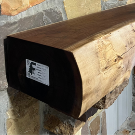 A live edge style fireplace mantel, made from walnut wood, mounted to a rock wall.