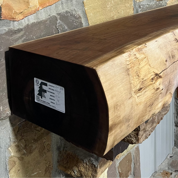 A live edge style fireplace mantel, made from walnut wood, mounted to a rock wall.