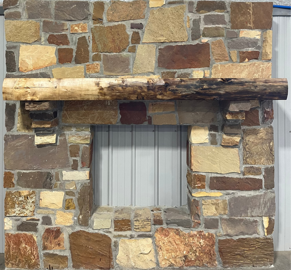 A live edge style fireplace mantel, made from walnut wood, mounted to a rock wall.