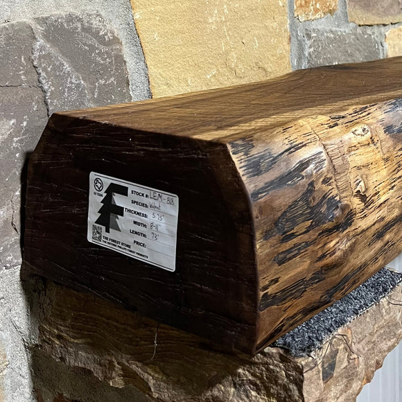 A live edge style fireplace mantel, made from walnut wood, mounted to a rock wall.