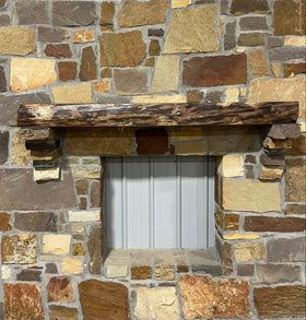 A live edge style fireplace mantel, made from walnut wood, mounted to a rock wall.