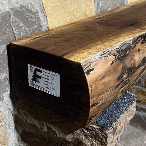 A live edge style fireplace mantel, made from walnut wood, mounted to a rock wall.