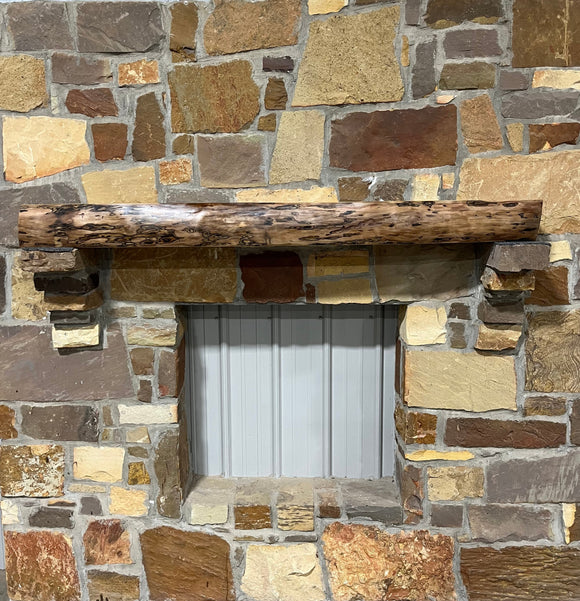A live edge style fireplace mantel, made from walnut wood, mounted to a rock wall.