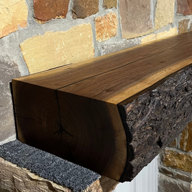 A live edge style fireplace mantel, made from walnut wood, mounted to a rock wall.