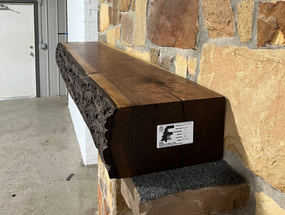 A live edge style fireplace mantel, made from walnut wood, mounted to a rock wall.