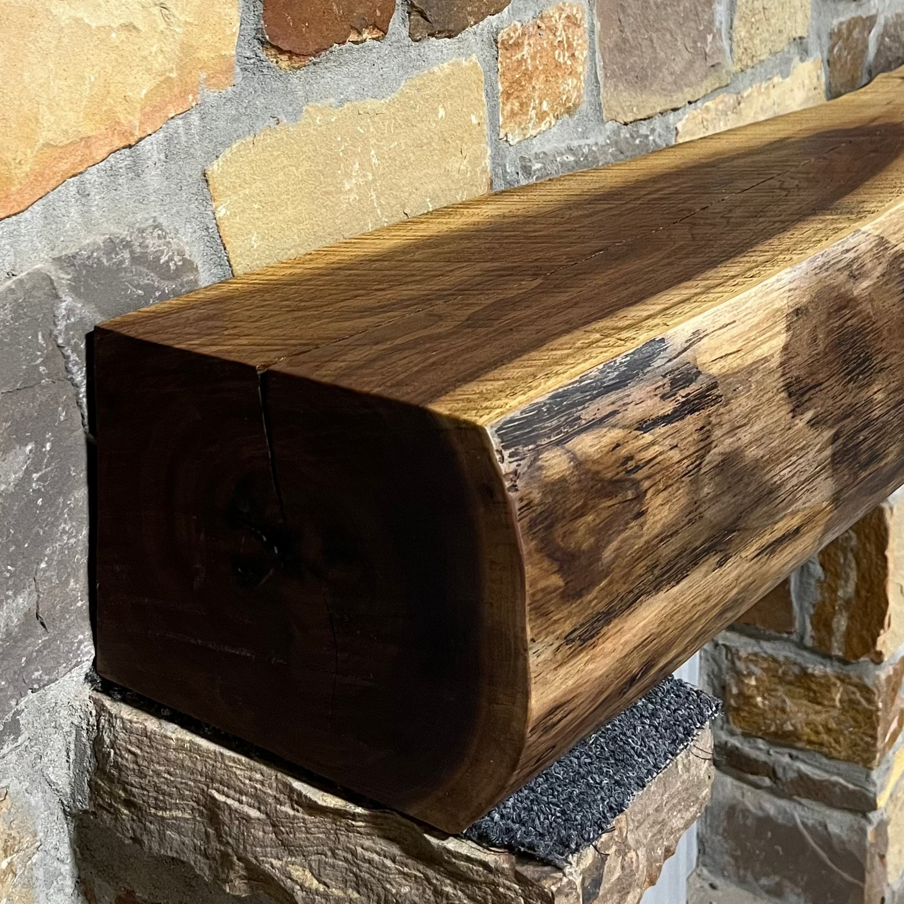 A solid walnut wood fireplace mantel with the side of the tree exposed on a stone wall.