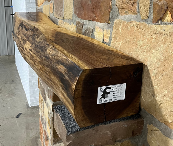 A live edge style fireplace mantel, made from walnut wood, mounted to a rock wall.