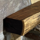 A live edge style fireplace mantel, made from walnut wood, mounted to a rock wall.