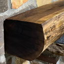 A live edge style fireplace mantel, made from walnut wood, mounted to a rock wall.