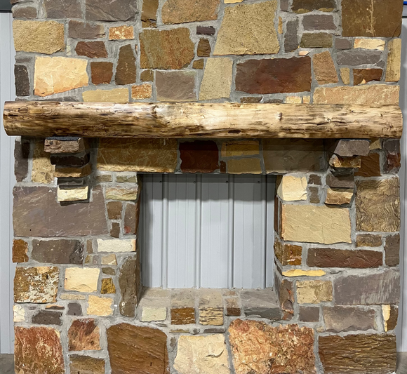 A live edge style fireplace mantel, made from walnut wood, mounted to a rock wall.