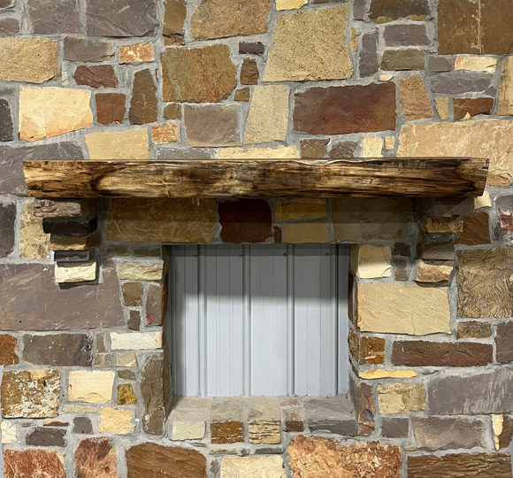 A live edge style fireplace mantel, made from walnut wood, mounted to a rock wall.