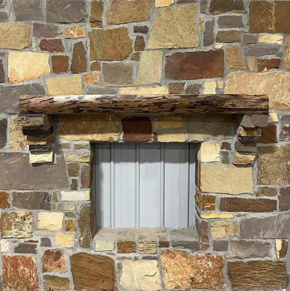 A live edge style fireplace mantel, made from walnut wood, mounted to a rock wall.