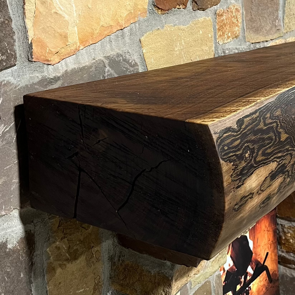 A live edge style fireplace mantel, made from walnut wood, mounted to a rock wall.