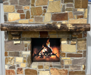A live edge style fireplace mantel, made from walnut wood, mounted to a rock wall.
