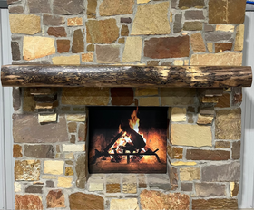 A live edge style fireplace mantel, made from walnut wood, mounted to a rock wall.