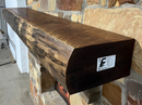 A live edge style fireplace mantel, made from walnut wood, mounted to a rock wall.