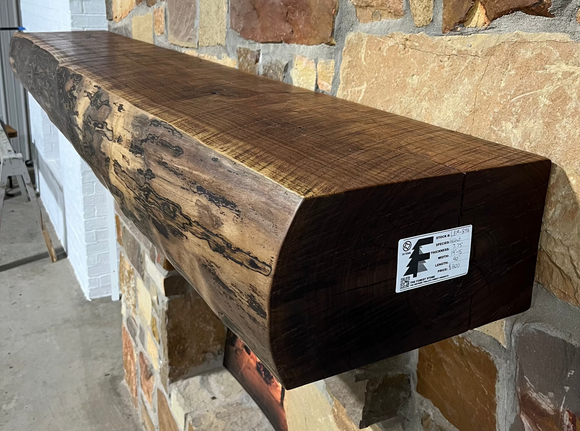 A live edge style fireplace mantel, made from walnut wood, mounted to a rock wall.