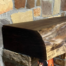 A live edge style fireplace mantel, made from walnut wood, mounted to a rock wall.