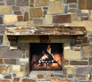 A live edge style fireplace mantel, made from walnut wood, mounted to a rock wall.