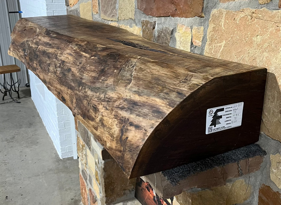 A live edge style fireplace mantel, made from walnut wood, mounted to a rock wall.
