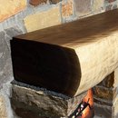 A live edge style fireplace mantel, made from walnut wood, mounted to a rock wall.