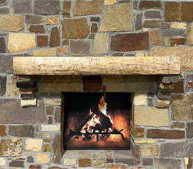 A live edge style fireplace mantel, made from walnut wood, mounted to a rock wall.
