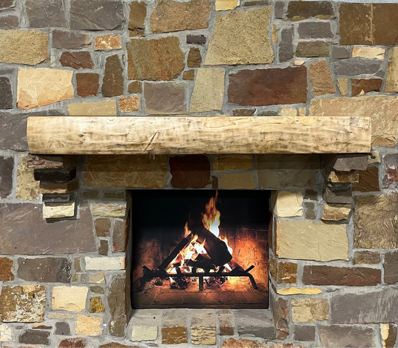 A live edge style fireplace mantel, made from walnut wood, mounted to a rock wall.