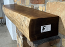 A live edge style fireplace mantel, made from walnut wood, mounted to a rock wall.