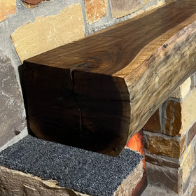 A live edge style fireplace mantel, made from walnut wood, mounted to a rock wall.