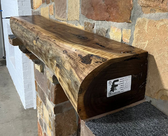 A live edge style fireplace mantel, made from walnut wood, mounted to a rock wall.