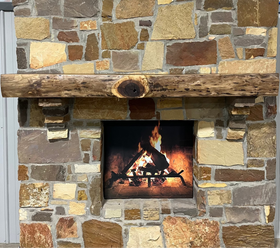 A live edge style fireplace mantel, made from walnut wood, mounted to a rock wall.