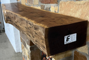 A live edge style fireplace mantel, made from walnut wood, mounted to a rock wall.