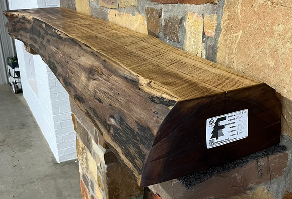A live edge style fireplace mantel, made from walnut wood, mounted to a rock wall.