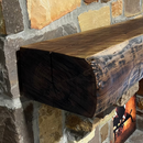 A live edge style fireplace mantel, made from walnut wood, mounted to a rock wall.