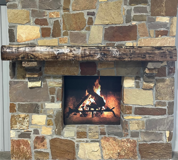A live edge style fireplace mantel, made from walnut wood, mounted to a rock wall.