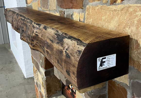 A live edge style fireplace mantel, made from walnut wood, mounted to a rock wall.