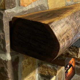 A live edge style fireplace mantel, made from walnut wood, mounted to a rock wall.