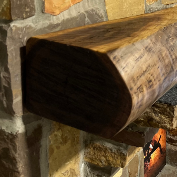 A live edge style fireplace mantel, made from walnut wood, mounted to a rock wall.