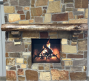 A live edge style fireplace mantel, made from walnut wood, mounted to a rock wall.