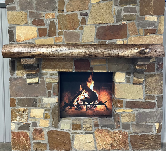 A live edge style fireplace mantel, made from walnut wood, mounted to a rock wall.