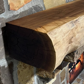 A live edge style fireplace mantel, made from walnut wood, mounted to a rock wall.