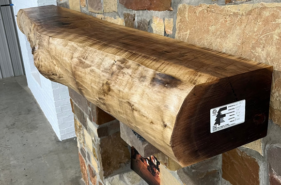 A live edge style fireplace mantel, made from walnut wood, mounted to a rock wall.