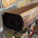 A live edge style fireplace mantel, made from walnut wood, mounted to a rock wall.