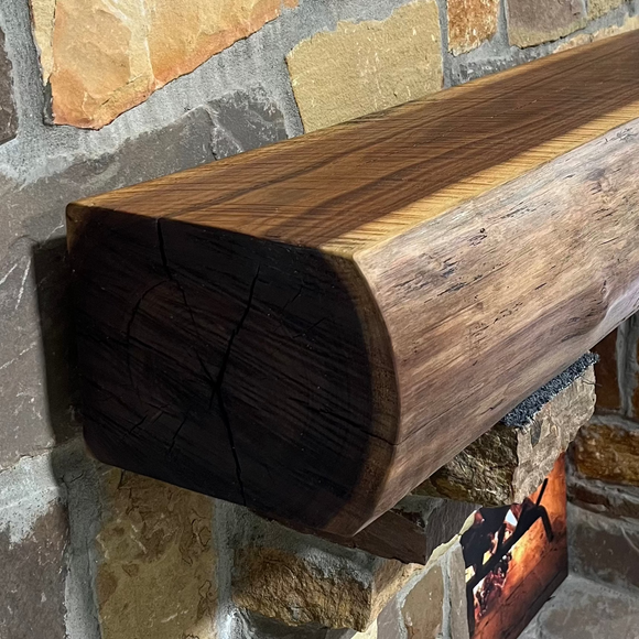 A live edge style fireplace mantel, made from walnut wood, mounted to a rock wall.