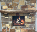 A live edge style fireplace mantel, made from walnut wood, mounted to a rock wall.