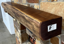 A live edge style fireplace mantel, made from walnut wood, mounted to a rock wall.