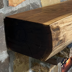 A live edge style fireplace mantel, made from walnut wood, mounted to a rock wall.