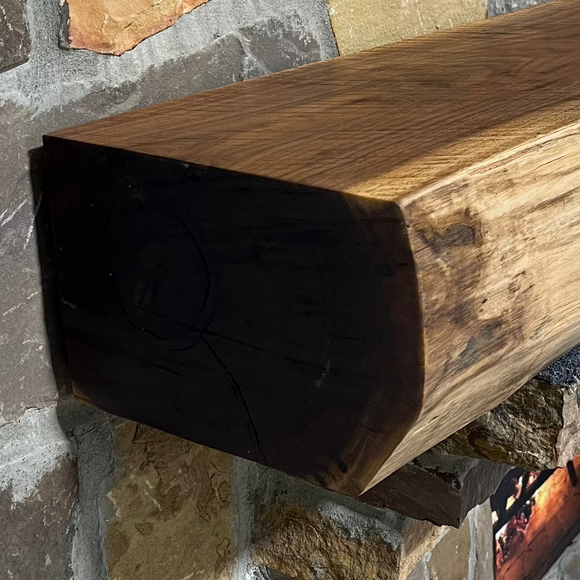 A live edge style fireplace mantel, made from walnut wood, mounted to a rock wall.