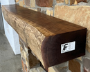 A live edge style fireplace mantel, made from walnut wood, mounted to a rock wall.