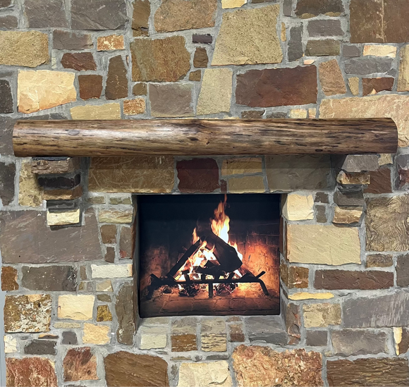 A live edge style fireplace mantel, made from walnut wood, mounted to a rock wall.